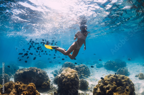 Woman glides underwater with yellow fins over sandy sea and coral. © artifirsov