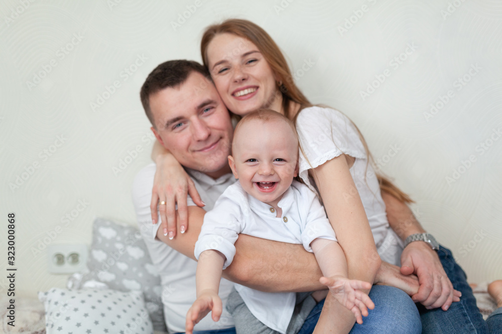 Portrait of a happy young family. Parents and baby hugging and playing on the sofa in the room Portrait of a happy young family. Parents and baby hugging and playing on the sofa in the room