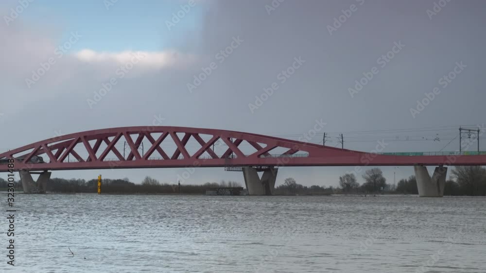 Water running over the floodplains of the river IJssel at the Hanzeboog train bridge during flooding in The Netherlands. A train is passing over the bridge in the distance. Water running over the floodplains of the river IJssel at the Hanzeboog train bridge during flooding in The Netherlands. A train is passing over the bridge in the distance.