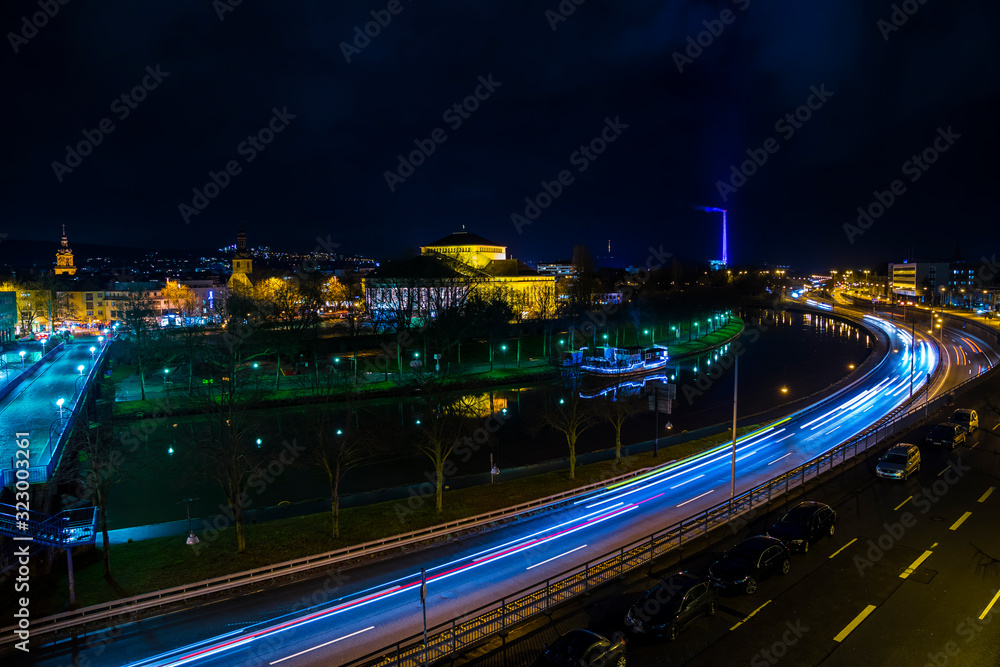 Germany, Magical night sky over roofs and busy highway street of downtown saarbrucken city by night with clouds, much traffic and starry sky