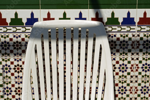 A white plastic chair (typical in holiday apartments in Europe) in front of a typical moorish / Andalusian tile wall