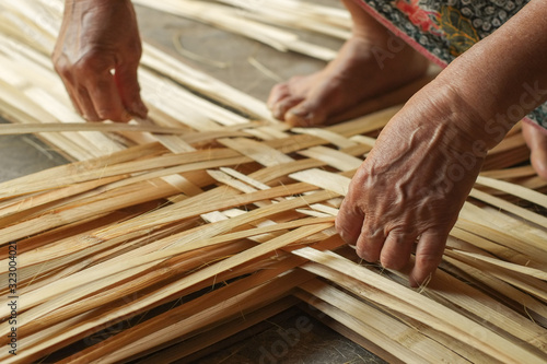 Hand elderly woman are weave bamboo strips of bottom of basket. © Jedsada Naeprai