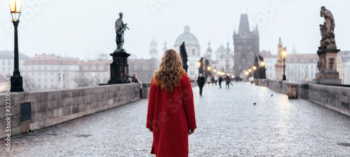 Female tourist walking alone on the Charles Bridge during the early morning in Prague, capital of Czech Republic