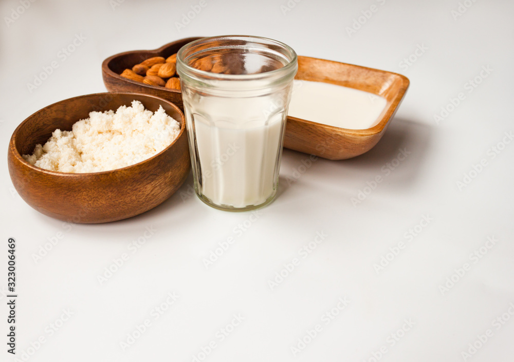 Homemade almond milk in a glass, almonds, milk and squeezed nut in wooden bowl on white background Homemade almond milk in a glass, almonds, milk and squeezed nut in wooden bowl on white background