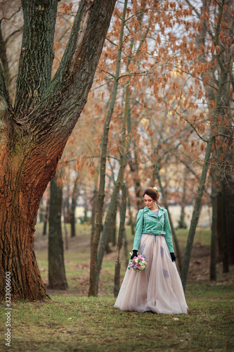 Young beautiful girl in a long dress and a green jacket and with bouquet of flowers in her hands