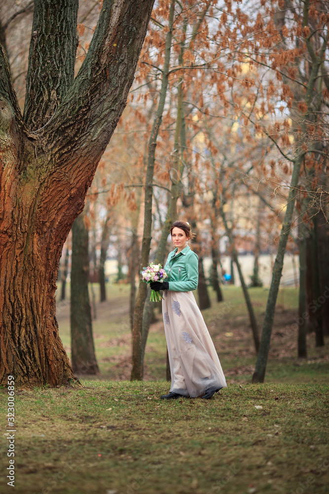 Young beautiful girl in a long dress and a green jacket and with bouquet of flowers in her hands