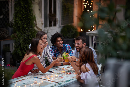 group of five adults making toast with cocktails, at the outdoor bar, laughing, having fun. Fun, party, socializing, multiethnic, introvert and extrovert persons concept photo
