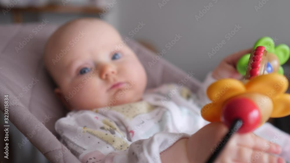 Baby Girl Sitting In Bouncer And Playing With Colorful Toys. Baby Girl Sitting In Bouncer And Playing With Colorful Toys.