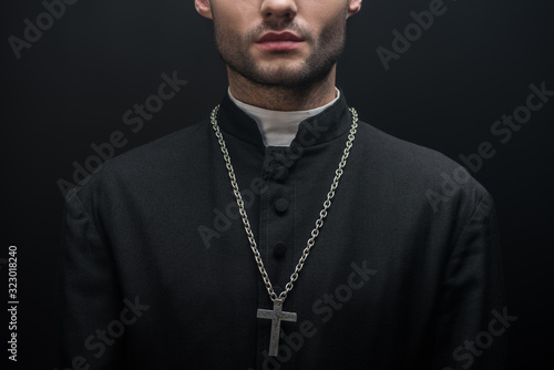 partial view of catholic priest with silver cross on necklace isolated on black