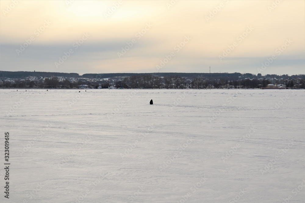 A frozen pond, snow, a fisherman, in the distance the city.