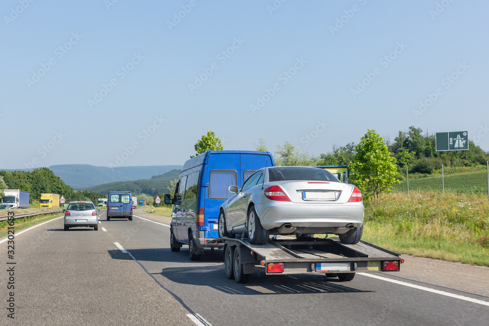 Car carrier trailer with car. Blue minibus with tow truck transporter carrying car on highway Car carrier trailer with car. Blue minibus with tow truck transporter carrying car on highway