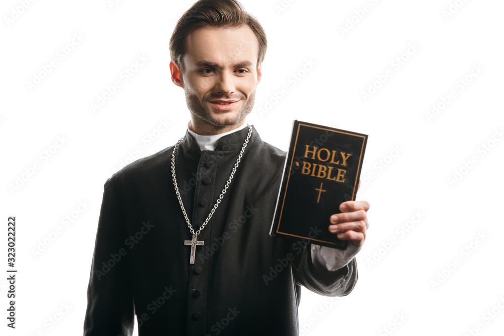 young catholic priest smiling while holding holy bible isolated on white young catholic priest smiling while holding holy bible isolated on white