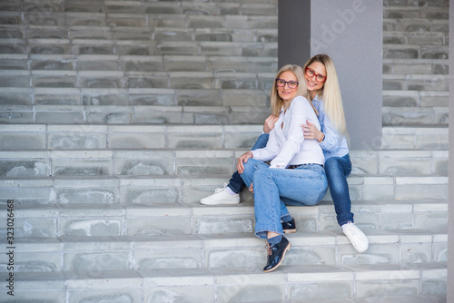 Fotografie A beautiful blonde with glasses and her mature mother are sitting on the stairs outdoor