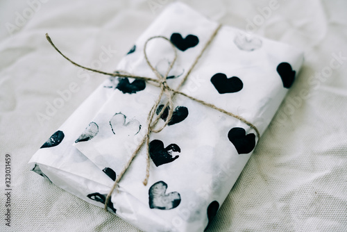a gift wrapped in homemade wrapping paper with black hearts tied with jute thread for Valentine's day on a white table