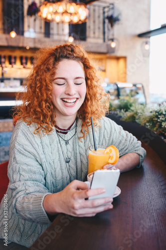 A young girl drinking orange smoothie and looking at her cell phone in a cafe.