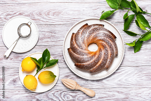 Homemade Gugelhupf cake with powdered sugar and organic lemon fruits on light wooden background. Flat lay. Copy space.