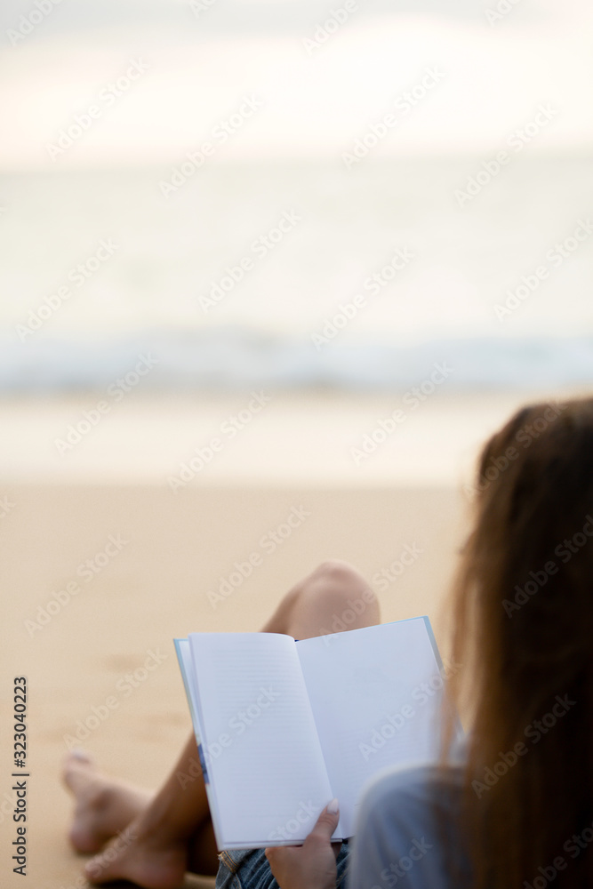 the brunette is lying on the beach in a shirt and denim shorts and reading an interesting book at sunset