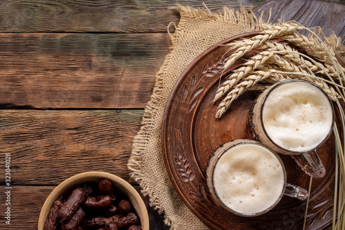 Frothy beer in the mug and sausages on brown wooden table background.