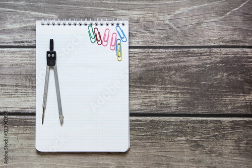 Notepad with a blank white sheet in a checker paper and with compass lies on the background of wooden boards