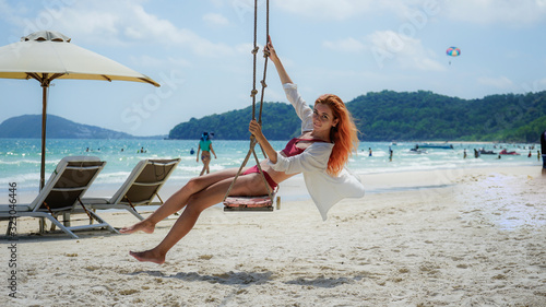 Beach summer vacation tropic palm style portrait of young beautiful girl on beach swing blue sea.Red haired woman swinging on the beach on Phu Quoc island, Vietnam. Happy on tropical palm tree swing.