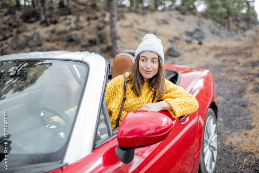 Portrait of a stylish woman in yellow sweater sitting on the driver's seat of convertible sports car on the roadside. Carefree lifestyle and traveling concept Portrait of a stylish woman in yellow sweater sitting on the driver's seat of convertible sports car on the roadside. Carefree lifestyle and traveling concept