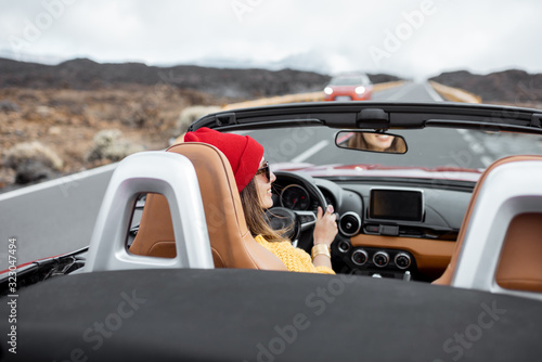 Young woman traveling by convertible car on the picturesquare road on the volcanic valley, rear view. Carefree lifestyle and travel concept