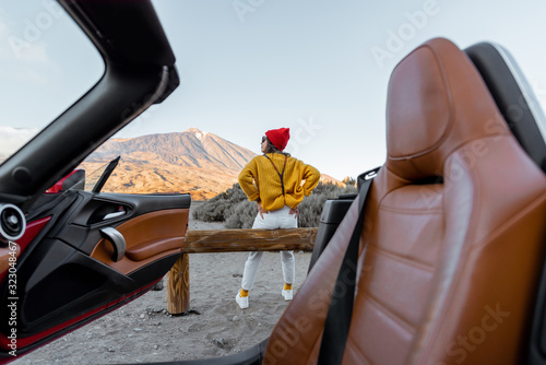 Woman dressed in bright sweater and hat enjoying great mountain landscapes during a sunset, traveling by car on the volcanic valley, wide view from the car intreior photo