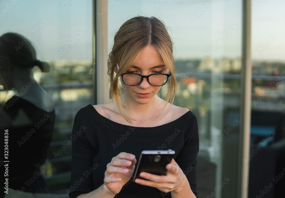 Young business woman uses phone. Good looking brunette female uses online banking on smart phone to transfer money from credit card. Girl using smart phone and chatting with business partners.