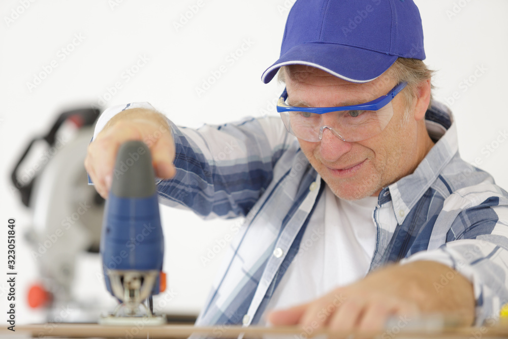 mature man carpenter builder working with electric jigsaw and wood