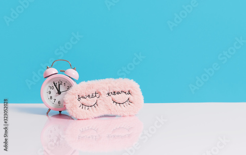 Sleep optimization. Pink fluffy mask for sleeping and a pink alarm clock on a light blue background. photo