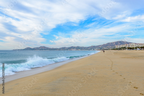 Fantastic ocean beach view with small figures of people and foot prints on sand. Cabo San Lucas. Mexico.