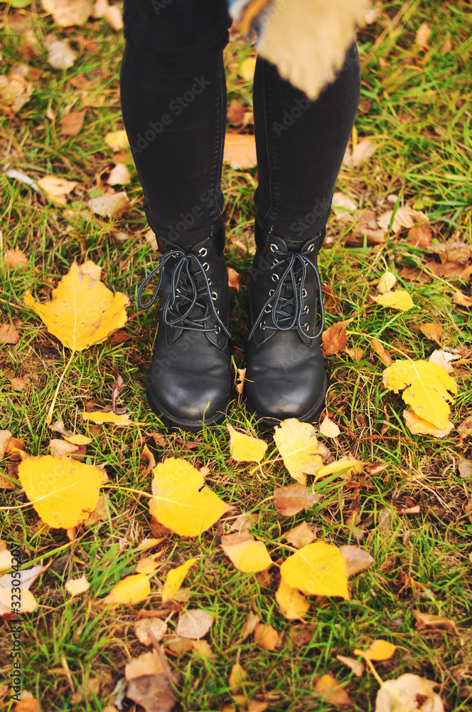 Women's black leather shoes stand on the ground covered with yellow autumn leaves. Lace up ankle boots for fall season. Women's black leather shoes stand on the ground covered with yellow autumn leaves. Lace up ankle boots for fall season.