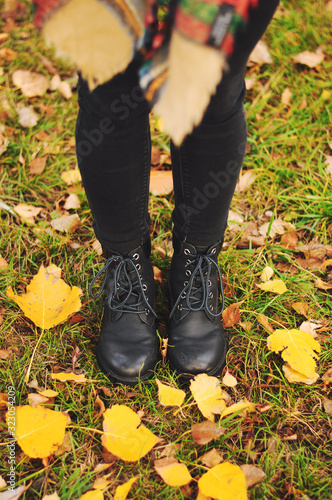Women's black leather shoes stand on the ground covered with yellow autumn leaves. Lace up ankle boots for fall season.