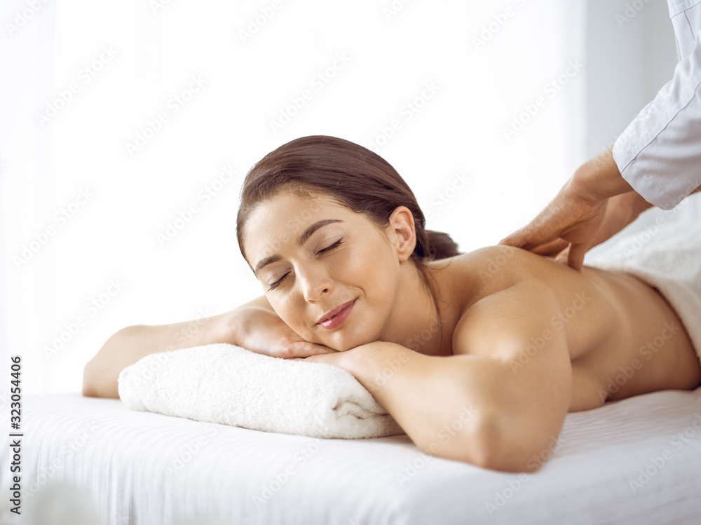 Beautiful brunette woman enjoying back massage with closed eyes. Spa and medicine concept
