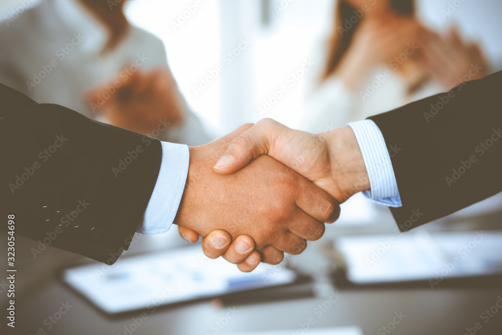 Business people shaking hands at meeting while theirs colleagues clapping and applauding. Group of unknown businessmen and women in modern white office. Success teamwork, partnership and handshake Business people shaking hands at meeting while theirs colleagues clapping and applauding. Group of unknown businessmen and women in modern white office. Success teamwork, partnership and handshake