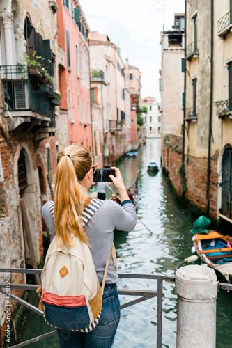 Young woman taking a photo on her smartphone of a canal in Venice, Italy