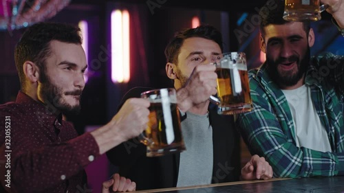 Smiling large young people three men in a pub drinking some beer from a big glasses they enjoying the atmosphere and spending a great time. Shot on ARRI Alexa Mini