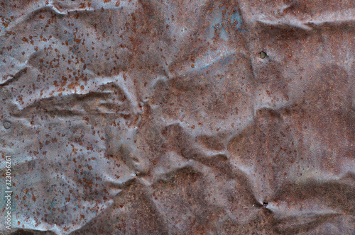 Close-up view of the crumpled rusty iron sheet with remnants of old paint and rust spots. Full frame image of the old weathered metal for texture or background, copy space