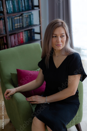 Blondie woman with long hair is posing in front of the bookshelves.