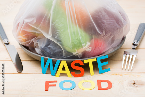 Stop wasting food. A bag of food waste on a plate and cutlery on a wooden table. Food waste concept. photo