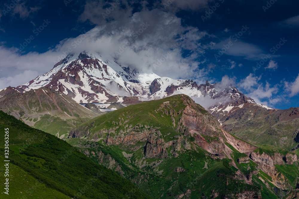Mount Kazbek in Georgia (Caucasus). Mountain peak covered with clouds and fog on a sunny and clear day.