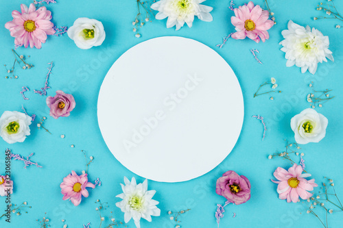 Blank round sheet of paper in center of blue background. Small sprigs, pink and white flowers are scattered around.Greeting card template. Happy mothers, women day, spring, easter concept.