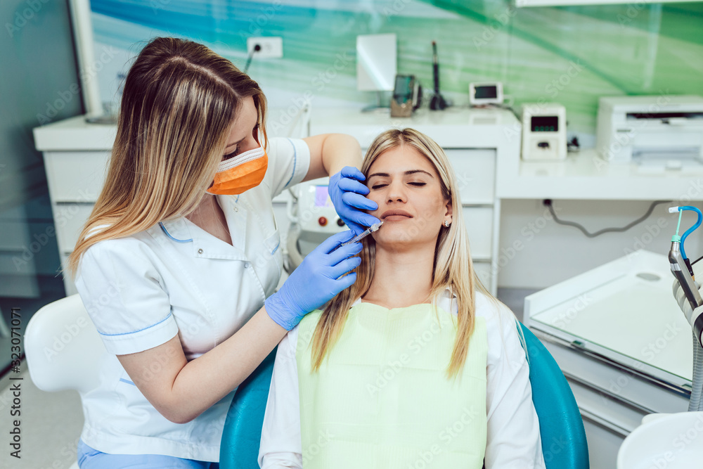 Attractive young woman is getting a rejuvenating injections. She is sitting calmly at clinic. The expert beautician is filling female lips by hyaluronic acid. Attractive young woman is getting a rejuvenating injections. She is sitting calmly at clinic. The expert beautician is filling female lips by hyaluronic acid.