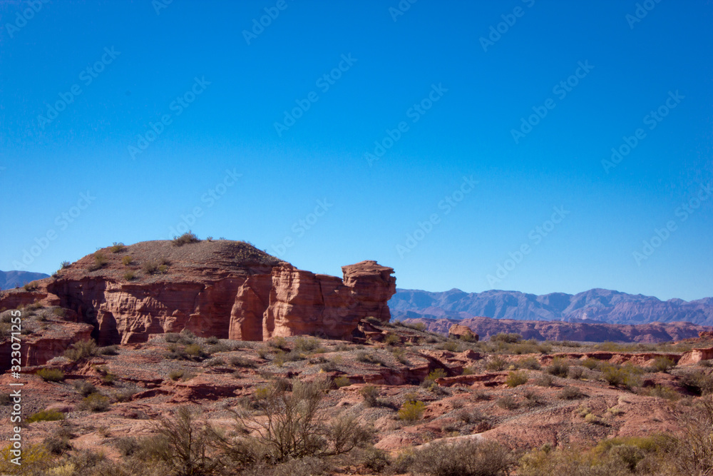 Red mountains in the desert with stone rock formations trees and green blue sky