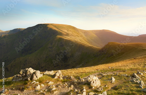 The warm evening glow as sunset approaches over the summit of High Street and the old Roman Road with Thornthwaite just to the right from the summit of Rampsgill Head in the Lake District UK.