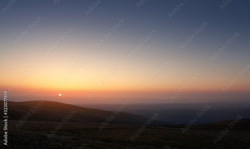 The pink, orange and blue skies of sunrise over Bampton Common from the summit of Rampsgill Head in the Lake Distict UK.
