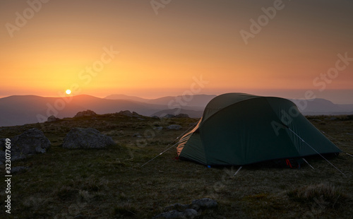 A tent pitched, camping on the mountain summit of Rampsgill Head with views of the surrounding mountains in the Lake District UK.