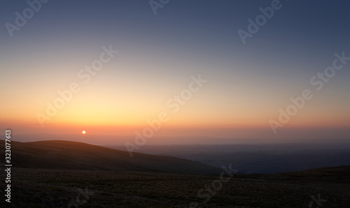 The pink, orange and blue skies of sunrise over Bampton Common from the summit of Rampsgill Head in the Lake Distict UK.