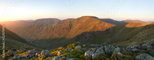 The warm morning glow of sunrise over the summit of High Street with Mardale Ill Bell and Harter Fell to the left from the summit of Rampsgill Head with the valley of Riggindale in the Lake District. photo