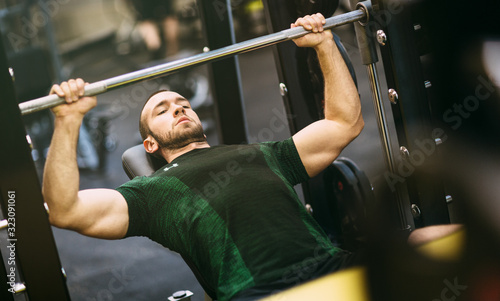 Fit athletic man pumping up muscles on bench press